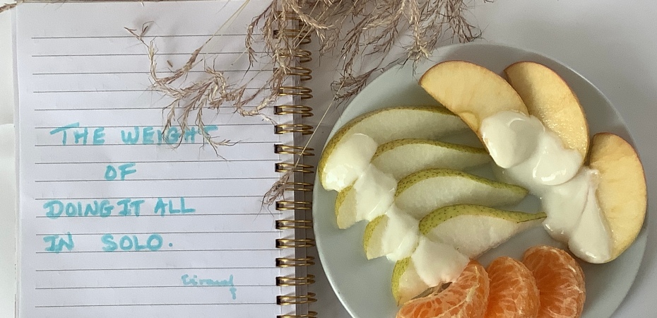 Text written in light sky blue on a spiral notebook and a plate with slices of pears, apples, and mandarins topped with yoghurt, and dried grass on a white background.