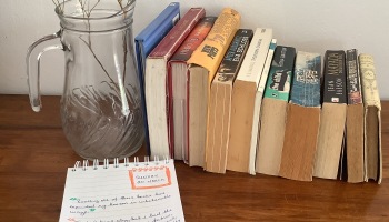 Notebook with handwritten quotes in from of row of books and dried flowers in transparent jar.