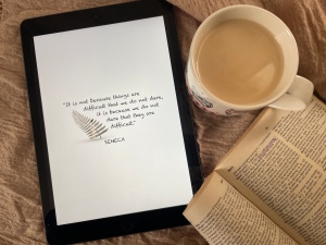 top view of tablet with motivational quote, mug of tea, and dictionary
